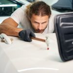 Guy smoothes out dents on door of a white car