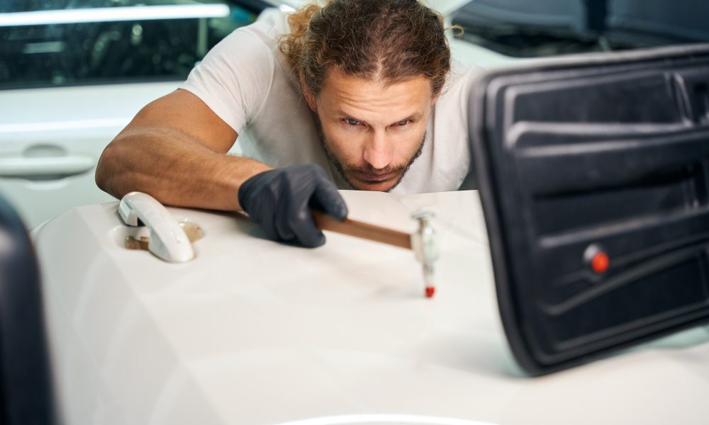 Guy smoothes out dents on door of a white car